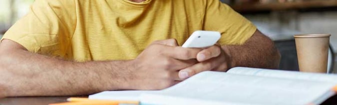 Man-in-yellow-shirt-researching-what-to-do-with-extra-money-on-his-cell-phone.