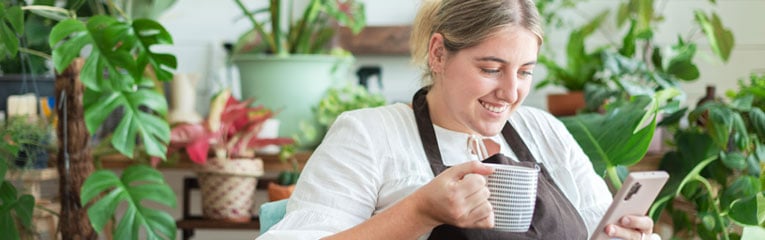 Business-owner-accessing-her-eStatements-using-her-money-management-tools-on-her-cell-phone-in-her-plant-store