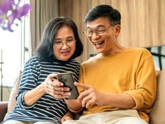 Asian-couple-looking-at-mortgage-rates-on-their-cell-phone-together-smiling.