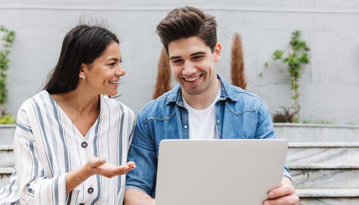 Couple exploring home equity loan possibilities on their laptop smiling while sitting on a bench.