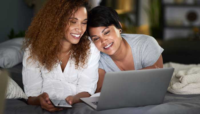 Women-couple-researching-what-to-do-with-extra-money-on-their-laptop-while-resting-their-heads-on-each-others-shoulders.