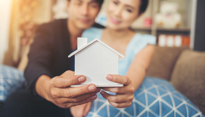 First-time-home-buyer-couple-holding-a-wood-home-representing-their-dream-of-homeownership.