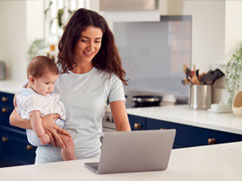 Mom-holding-her-baby-using-a-mortgage-affordability-calculator-on-her-laptop-in-her-kitchen.