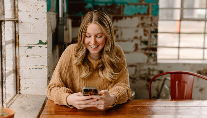 Young-woman-accessing-her-online-and-mobile-banking tools-on-her-cell-phone-at-a-restaurant.